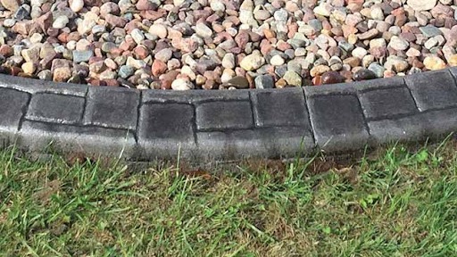 Durable Concrete Curbing: Long-Term Value for Twin Cities Homes 3 A curved border of durable concrete curbing made from dark rectangular stones separates a patch of grass from an area covered with multicolored pebbles, adding long-term value to Twin Cities homes.