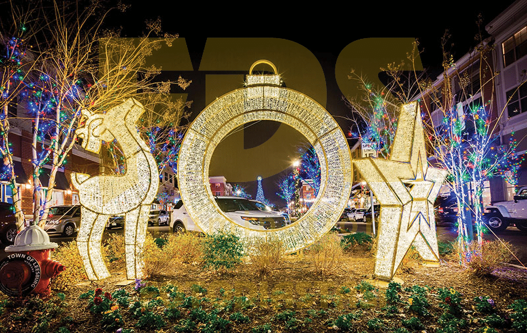 Illuminated holiday decorations shaped like a reindeer, ornament, and star spelling "JOY" brighten the Twin Cities night, with festive lights from a dazzling Holiday Light Installation on nearby trees and buildings.