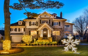 Showcase Gallery: Large house decorated with white holiday lights, illuminated bushes, and a large lit snowflake decoration on the front lawn at dusk.