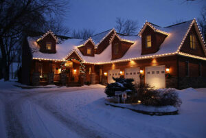A house with snow-covered roof and yard, decorated with white string lights along the roofline and porch, lit warmly at dusk, creates a picturesque Showcase Gallery perfect for winter evenings.