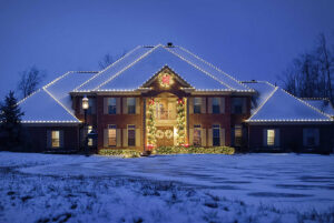 A large brick house with snow on the roof and ground, decorated with white Christmas lights and wreaths at dusk, creates a perfect Showcase Gallery of festive charm.