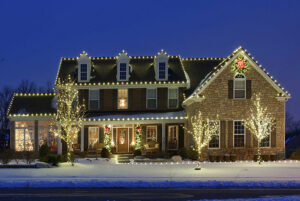 A two-story house with snow on the ground, decorated with white holiday lights on the roof, trees, and windows at dusk—a true Showcase Gallery of festive cheer.