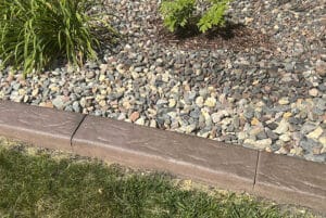 A concrete landscape edging separates green grass from decorative rocks and plants, creating a clean border worthy of any Showcase Gallery.