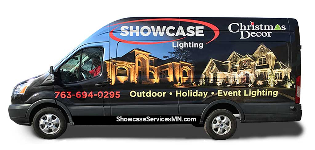 Side view of a Showcase Lighting van wrapped with images of illuminated houses and text promoting outdoor, holiday, and event lighting services. Contact number and website are displayed.
