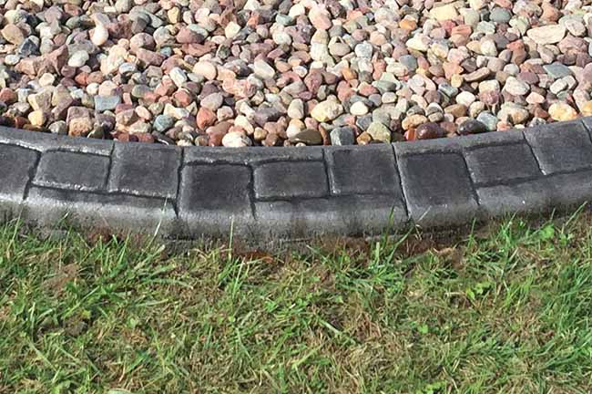 Curved stone border separates a section of decorative rocks from a grassy lawn.