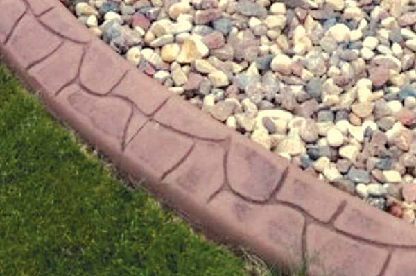 A curved concrete garden edging separates a patch of green grass from an area covered with multi-colored small rocks.