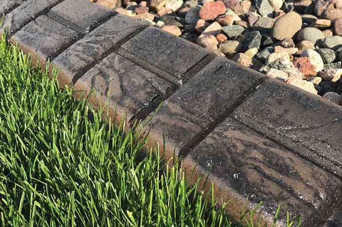 Close-up of a concrete landscape edging separating green grass from a bed of assorted rocks.