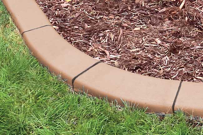 A concrete garden edging separates green grass from a mulched area, with visible seams between edging segments.