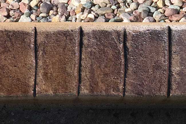 Close-up of a concrete curb with four vertical expansion joints, with small rocks visible in the background.